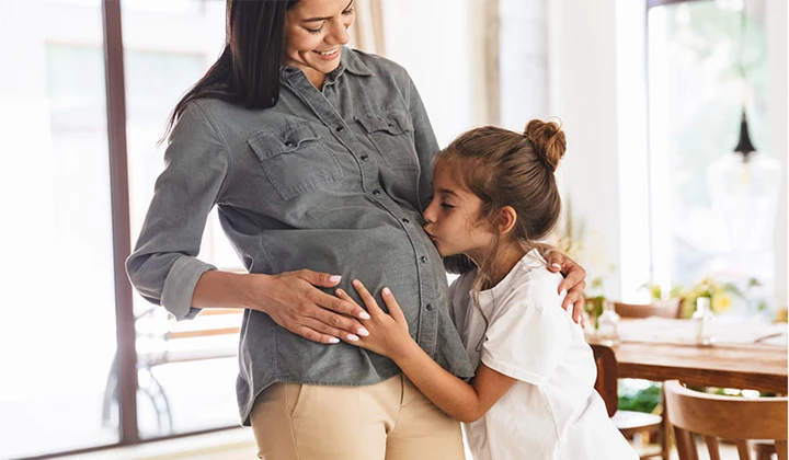 Mädchen küsst Bauch der schwangeren Mutter Vitaminmangel bei Schwangeren