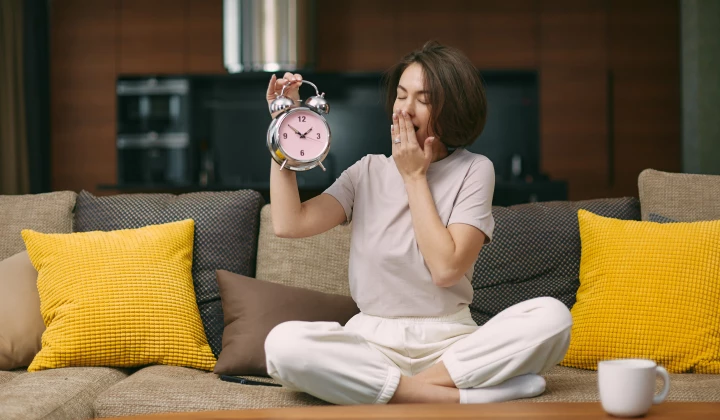 Frau hält Wecker und gähnt Frau hält Wecker und gähnt