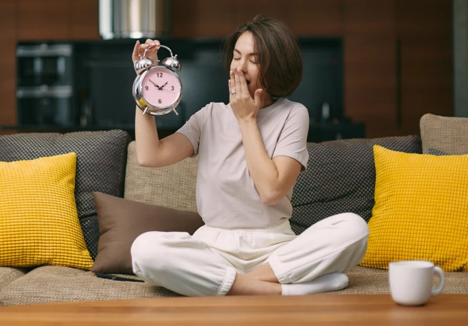 Frau hält Wecker und gähnt Frau hält Wecker und gähnt